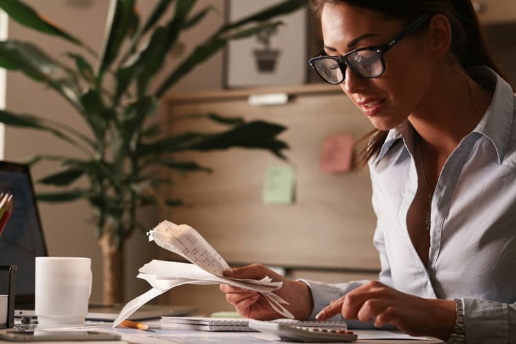 Small business owner at her desk going through receipts with a calculator, working out what website maintenance costs