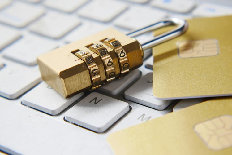 Brass combination padlock sitting on a white laptop keyboard next to gold credit cards, illustrating a website security audit